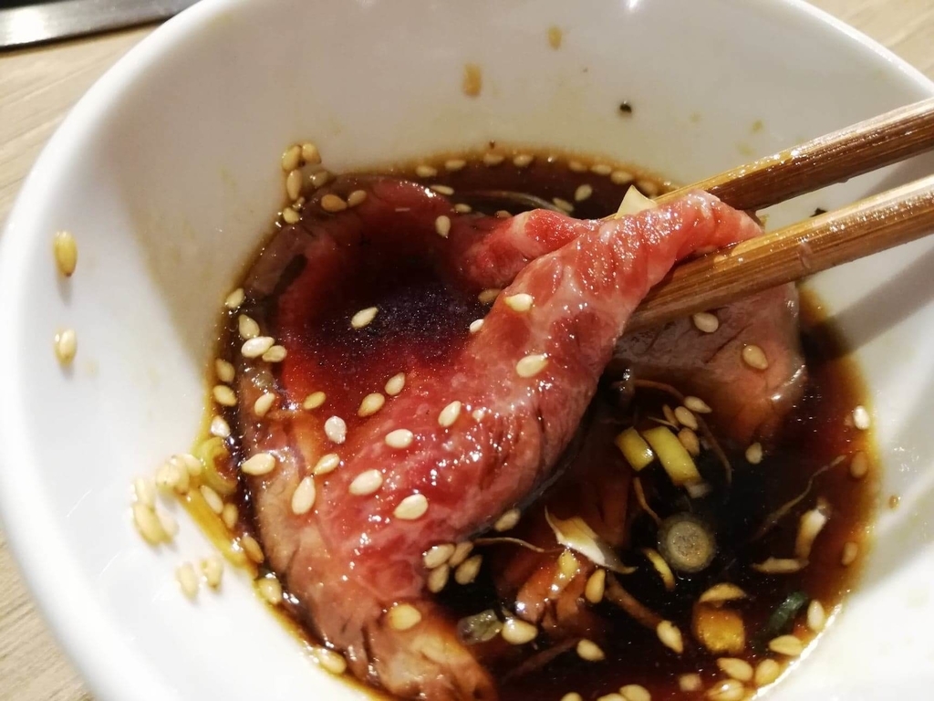 浅草焼肉たん鬼『鬼く丼』のお肉を、醤油ダレにつけている写真