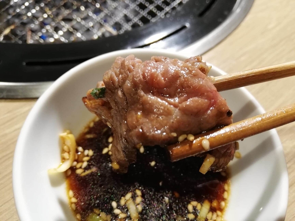 浅草焼肉たん鬼『鬼く丼』の焼いたお肉を醤油ダレにつけている写真