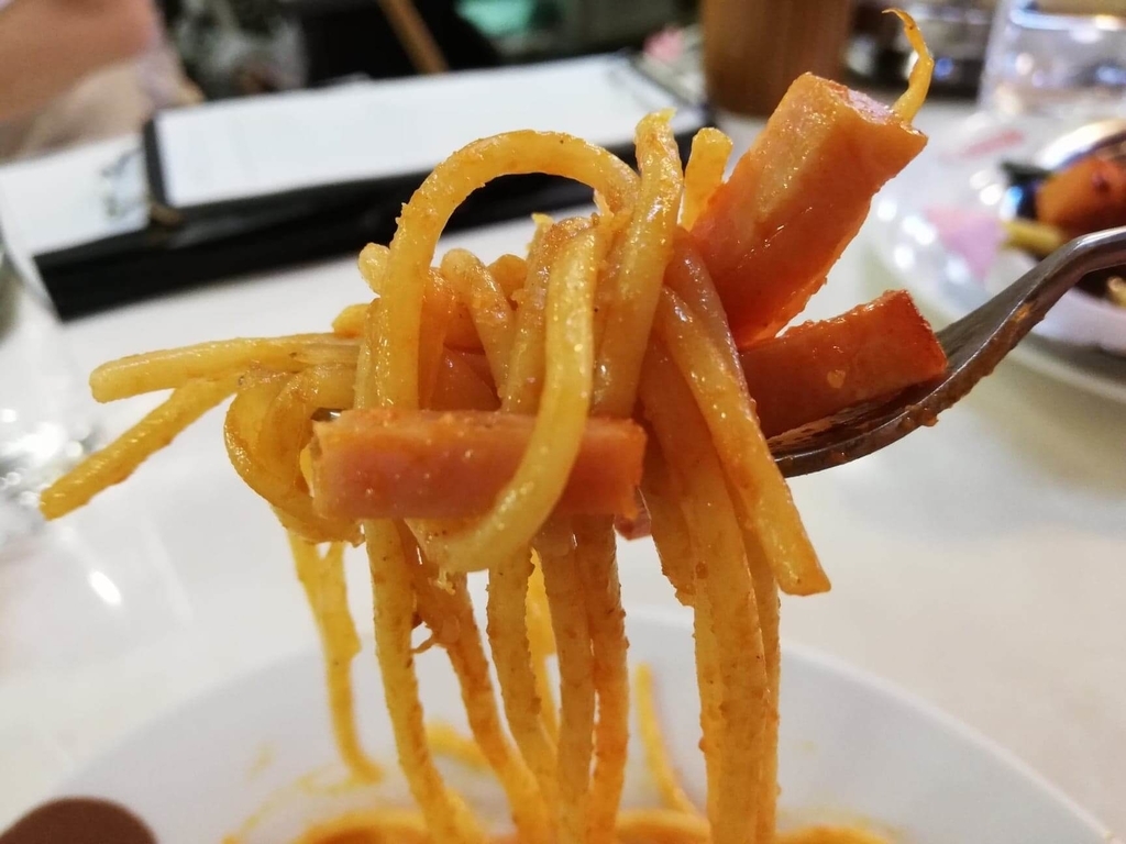 浅草『洋食屋ヨシカミ』のスパゲティーの麺を、ベーコンと一緒にフォークで持ち上げた写真