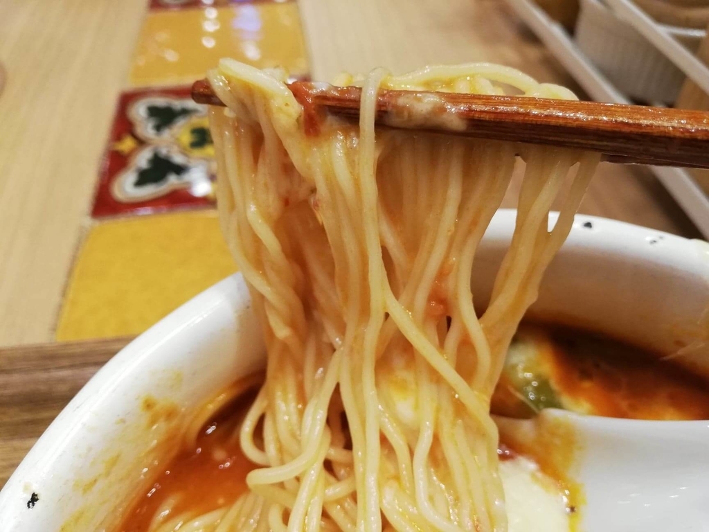 新宿ミロード店『太陽のトマト麺withチーズ』の、太陽のチーズラーメンの麺を箸で持ち上げた写真