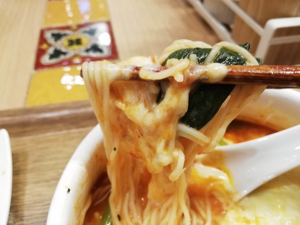 新宿ミロード店『太陽のトマト麺withチーズ』の、太陽のチーズラーメンの麺とほうれん草を箸で持ち上げた写真