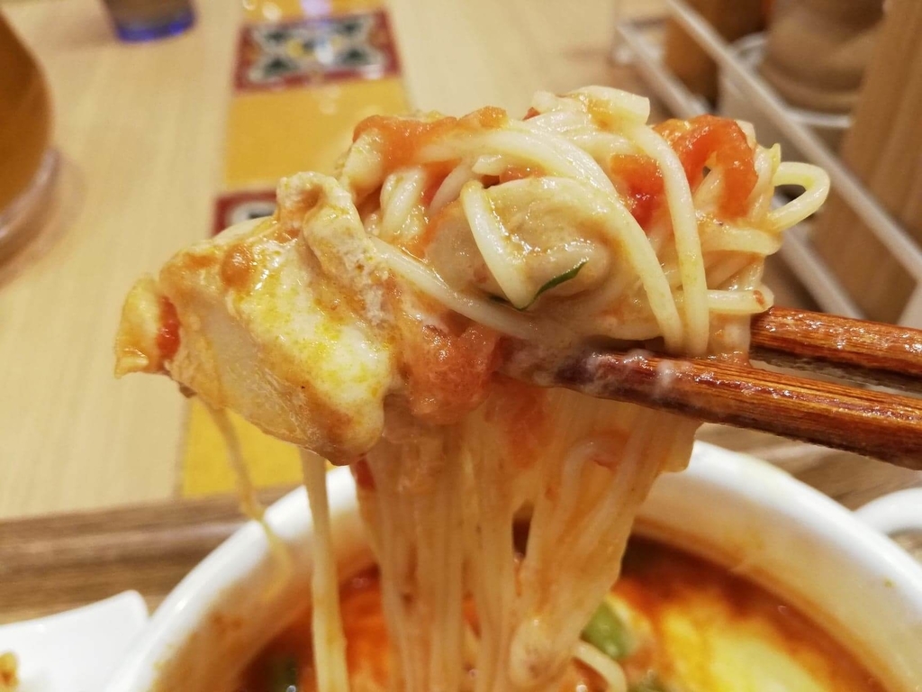 新宿ミロード店『太陽のトマト麺withチーズ』の、太陽のチーズラーメンの麺とチキンを箸で掴んだ写真