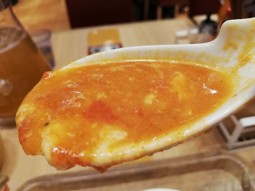 新宿ミロード店『太陽のトマト麺withチーズ』の、太陽のチーズラーメンのスープとチーズをレンゲで持ち上げた写真