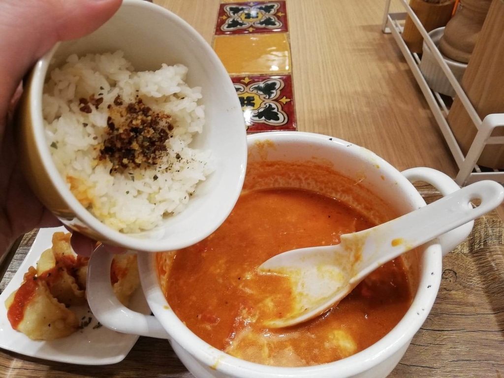 新宿ミロード店『太陽のトマト麺withチーズ』の、太陽のチーズラーメンにライスを入れている写真