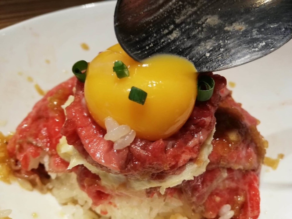 新宿『焼肉ブルズ』の特選和牛のローストビーフ丼の黄身を割っている写真
