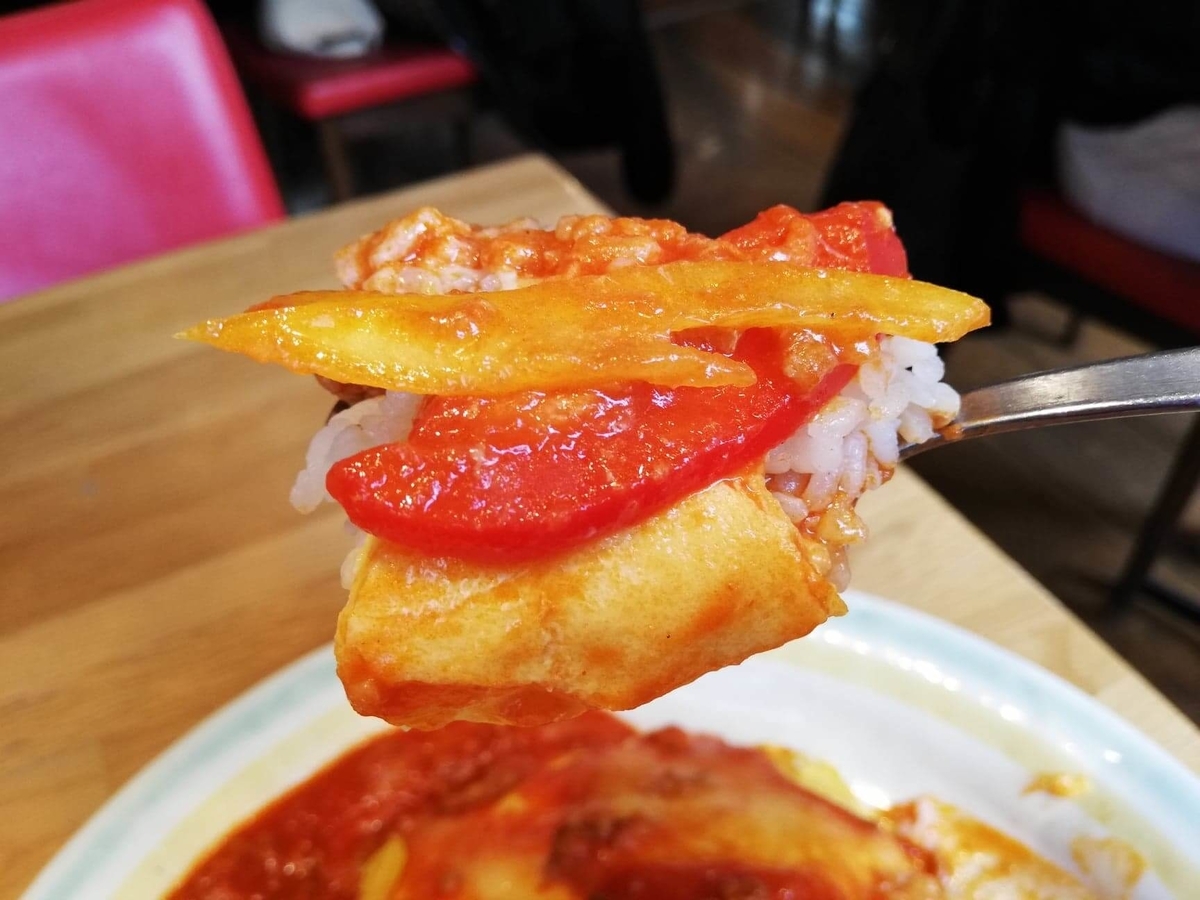 渋谷『ポムの樹』の、アボカドとモッツァレラチーズのトマトミンチオムライスにパプリカを乗せてスプーンですくった写真