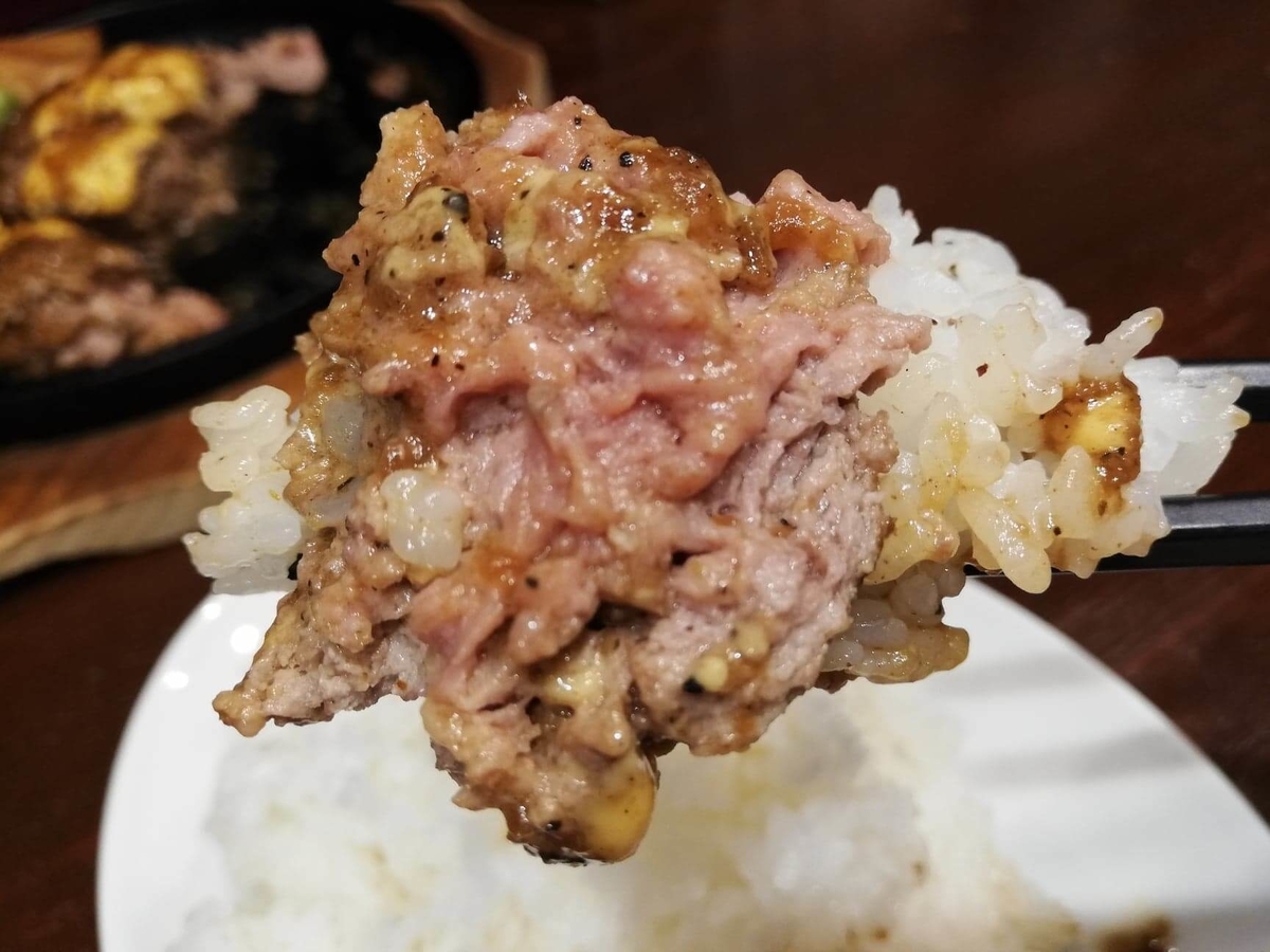 池袋『札幌牛亭』の、平日ランチタイム限定ハンバーグステーキセットのハンバーグを、ライスと一緒に箸で掴んでいる写真