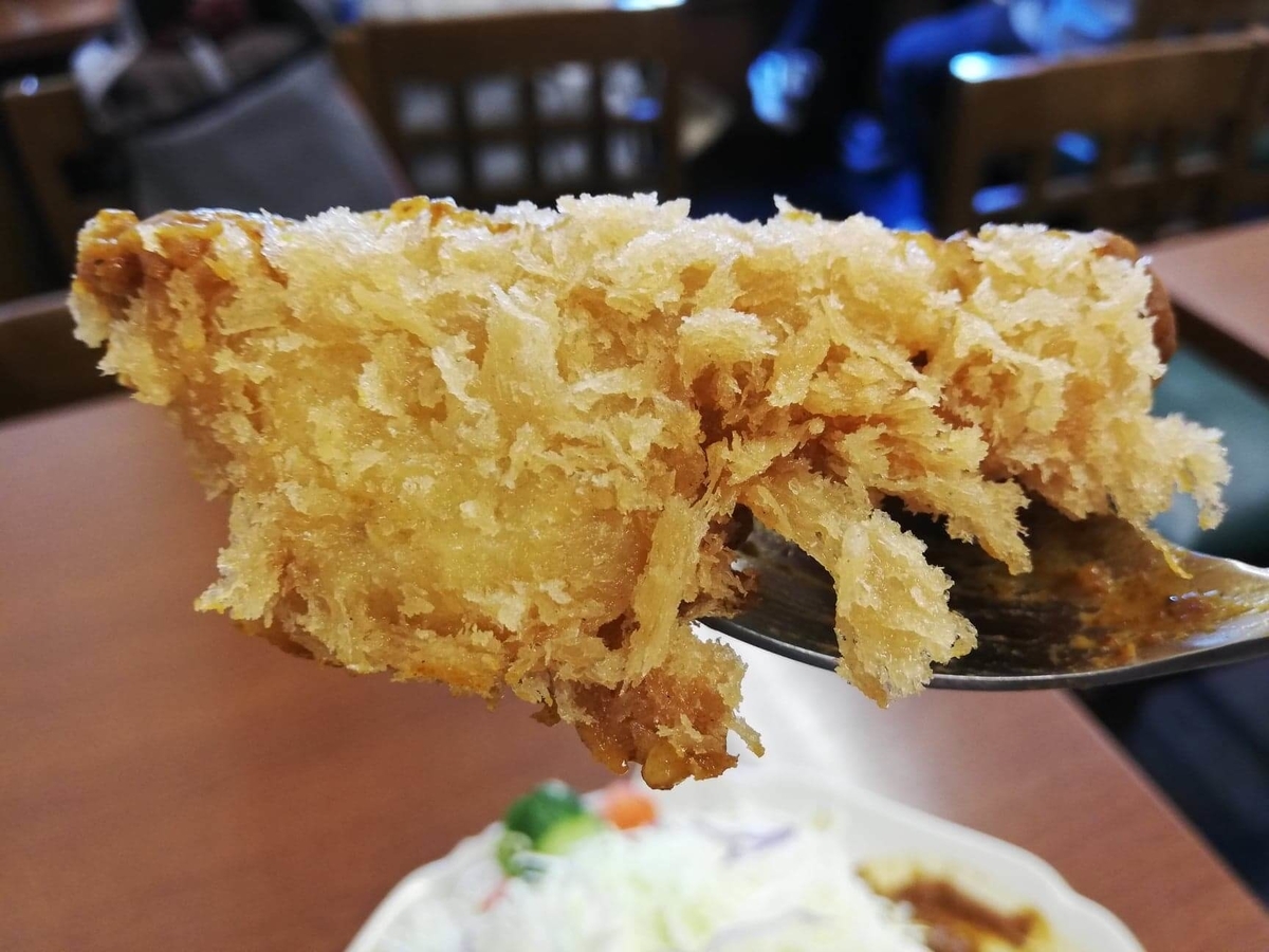 池袋『とんかつ清水屋』のロースかつカレー定食のロースカツを、スプーンですくった写真