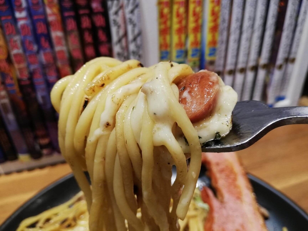 立川『スパゲッティPiaPia（ピアピア）』の、豚にんにくスパゲッティの麺とウィンナーをフォークですくっている写真