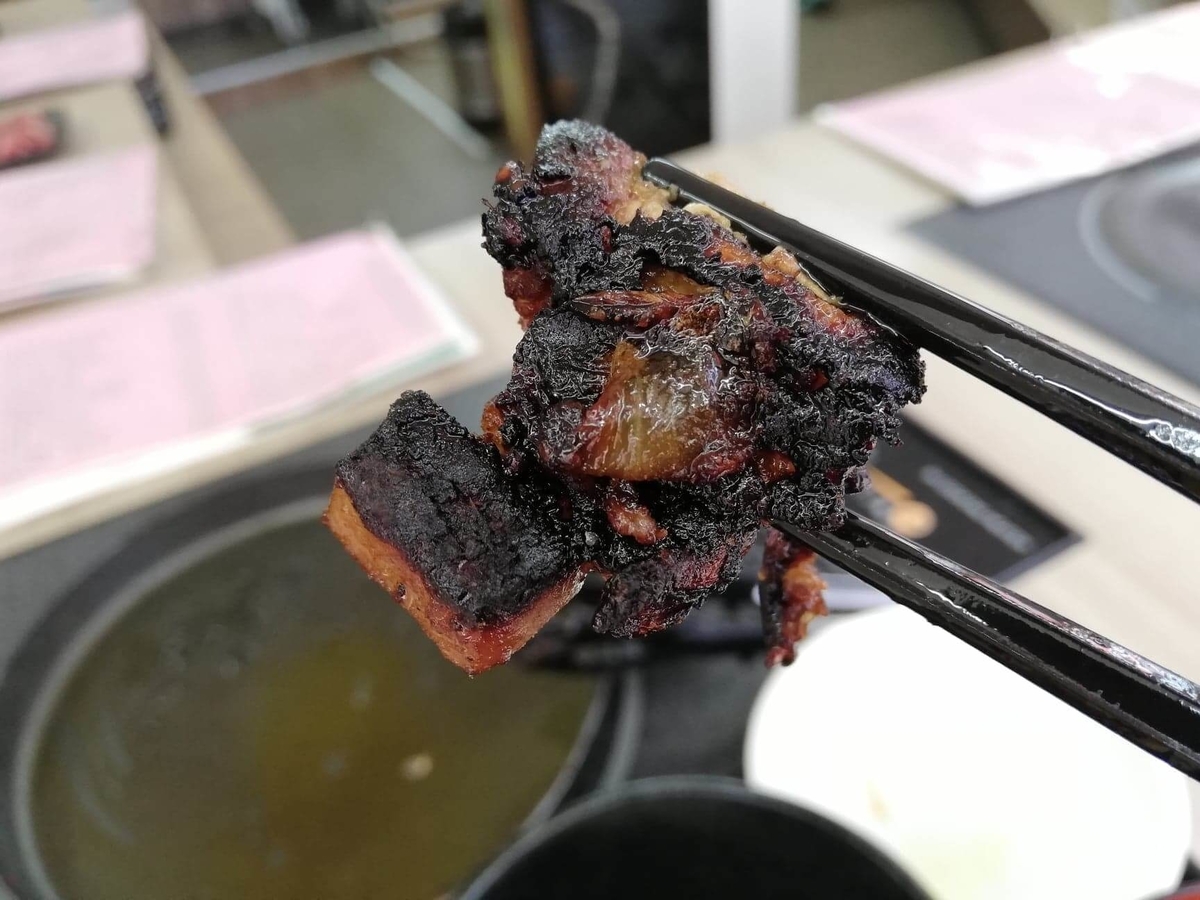 江古田『ふくふく食堂』のBBQ定食の焦げ肉を箸で掴んでいる写真