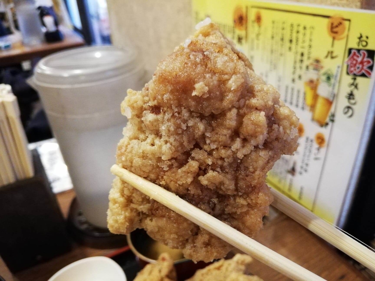 立川『ひなたかなた』のデカ盛り唐揚げ丼の唐揚げを、箸で掴んでいる写真