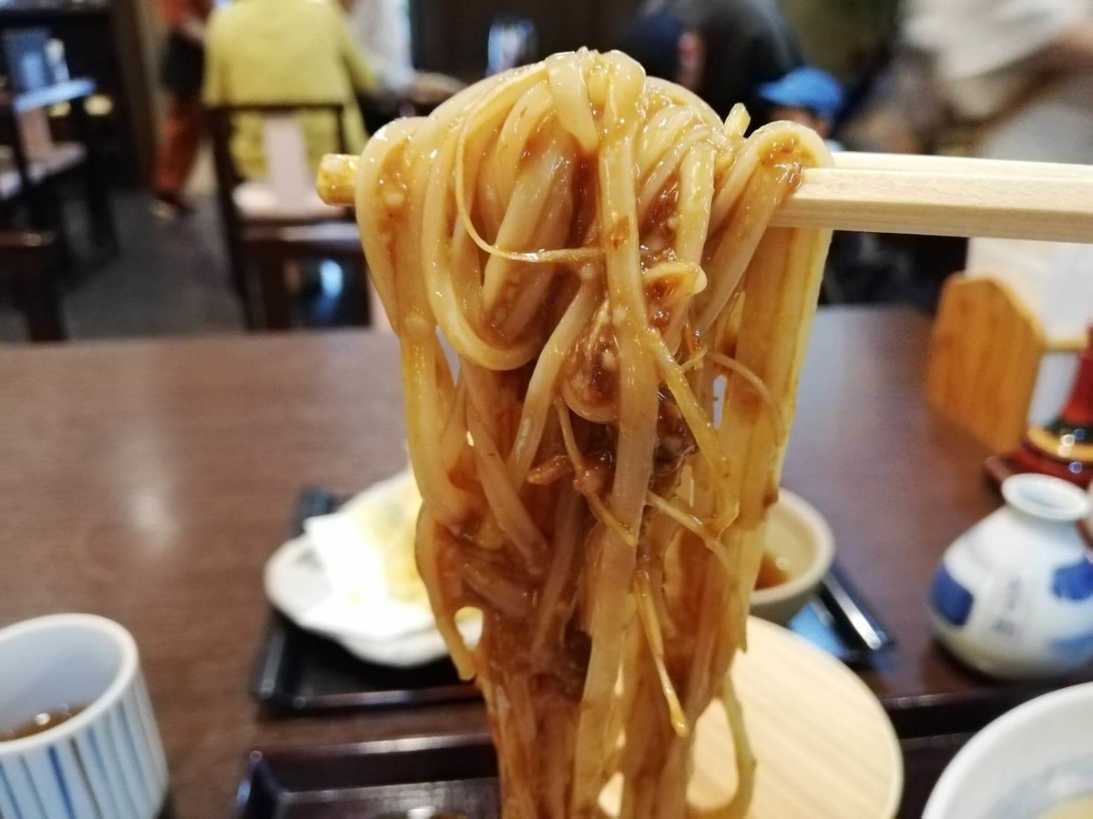 稲庭うどん『佐藤養助』秋田店の、肉味噌をつけたうどんを箸で掴んでいる写真