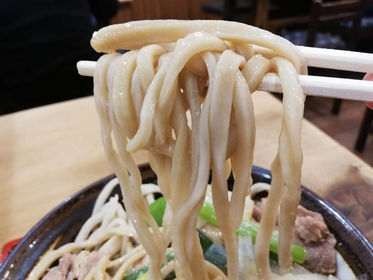 『浅草角萬』の冷やし肉南蛮の麺を、箸で持ち上げている写真