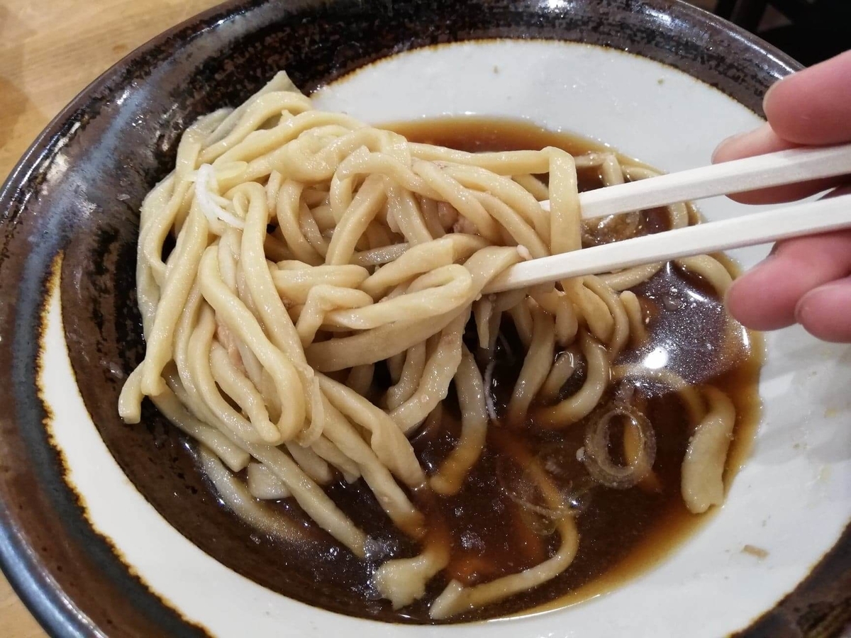 『浅草角萬』の冷やし肉南蛮の麺を、箸で持ち上げている写真