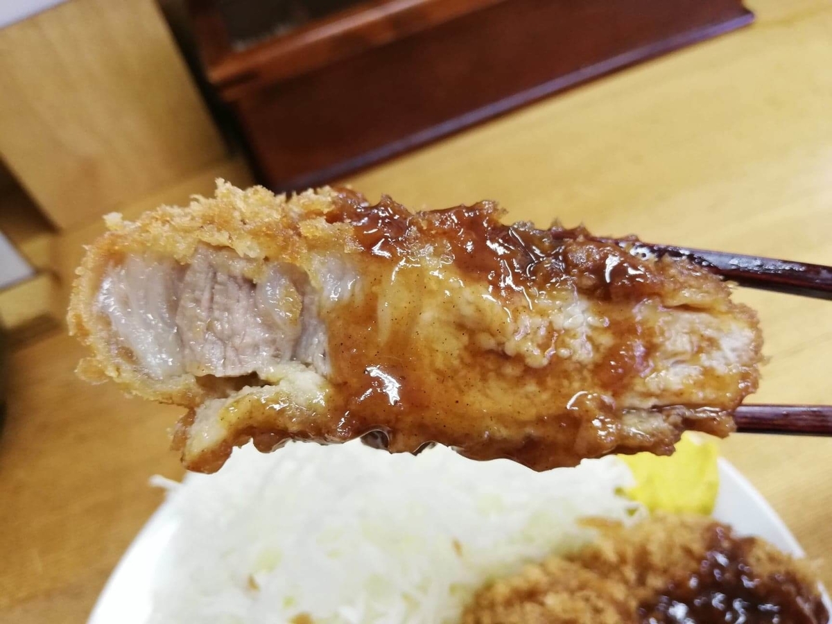 高田馬場『とんかついちよし』のロースかつにソースをかけて、箸で持ち上げている写真