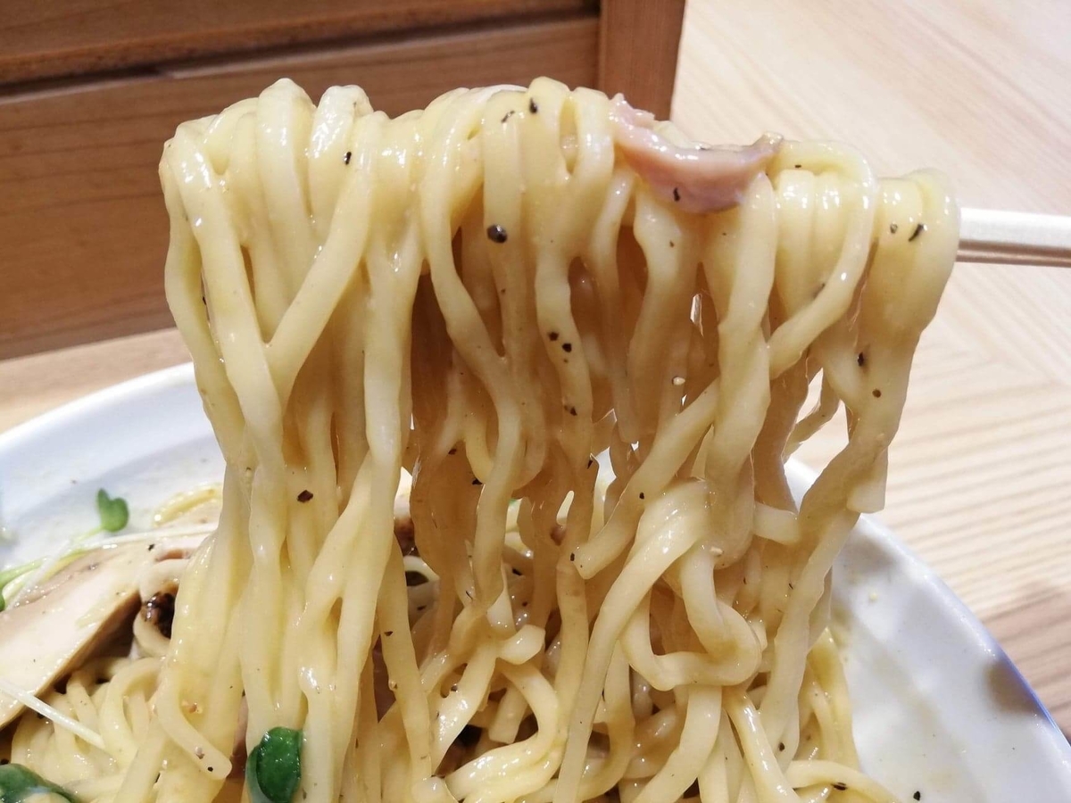 秋津（新秋津）『麺場二寅』の鶏ボナーラの麺を箸で持ち上げている写真