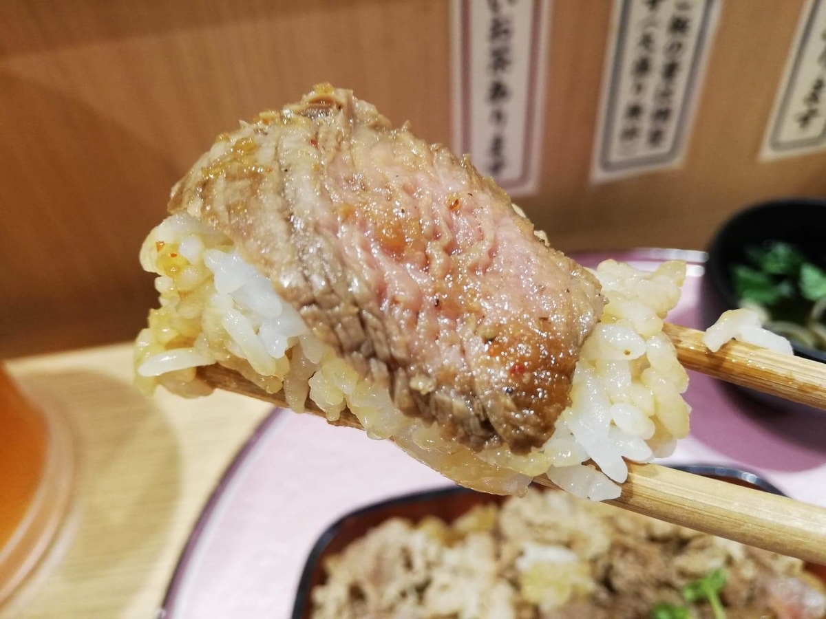 大阪『ビフテキ重・肉飯 ロマン亭』のビフテキとライスを箸で掴んでいる写真