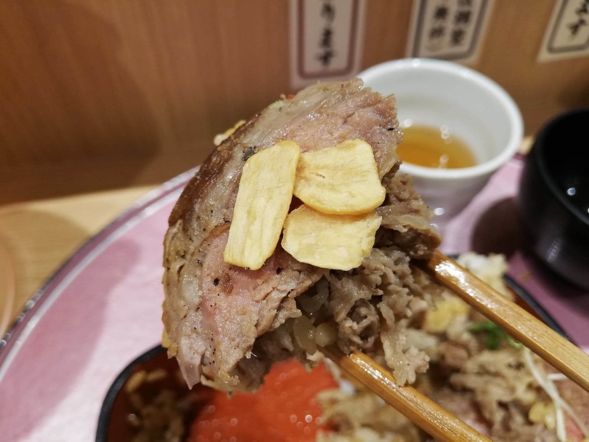 大阪『ビフテキ重・肉飯 ロマン亭』のビフテキにガーリックを乗せた写真