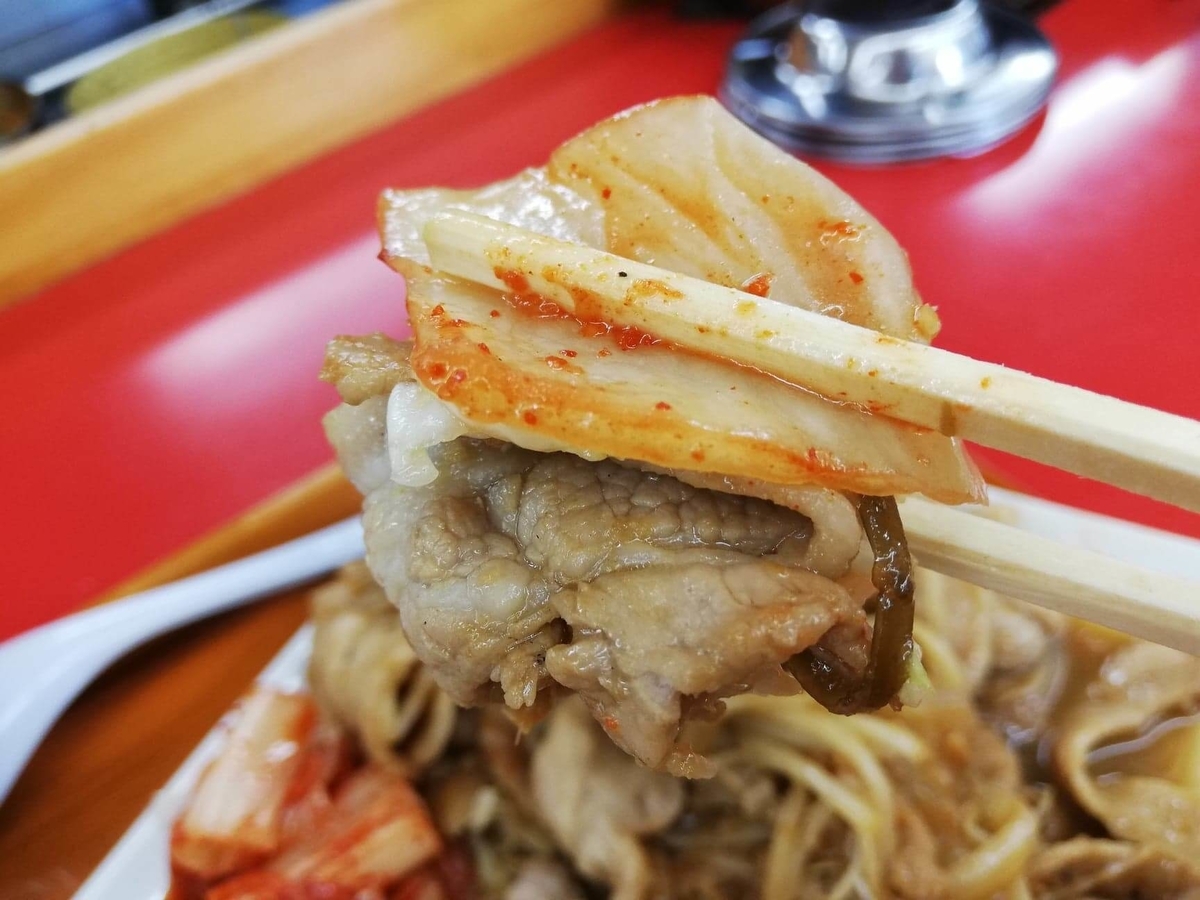 新座『くるまやラーメン』の焼肉とキムチを箸で持ち上げている写真